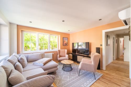 Moderna sala de estar en el apartamento Les Ambrades en Kaysersberg con paredes melocotón, cómoda decoración, televisor y ventanales amplios