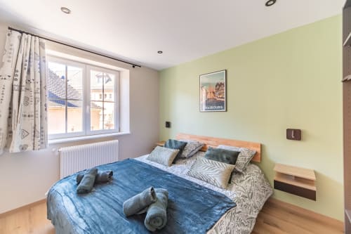 Habitación luminosa en Les Ambrades con ropa de cama azul, paredes amarillas y cartel del patrimonio de Estrasburgo en Kaysersberg
