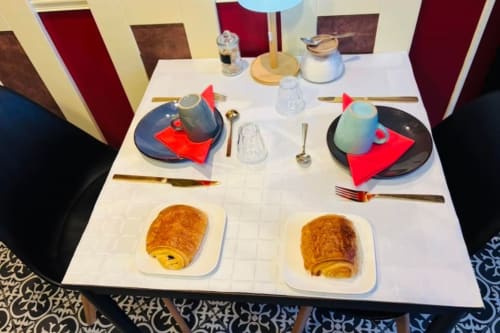 Table de petit-déjeuner élégamment dressée pour deux à Au Richebourg Nogent, avec croissants et couverts aux accents rouges