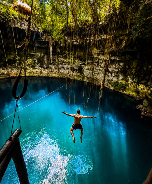 Hombre saltando desde un acantilado hacia el cenote turquesa del Hotel Boutique Cenote Secreto Maya, Valladolid Yucatán