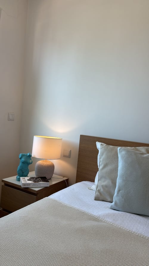 Modern bedroom with wooden bed, beige pillows, nightstand with turquoise sculpture and lit lamp at Sesimbra Sun Sea villa
