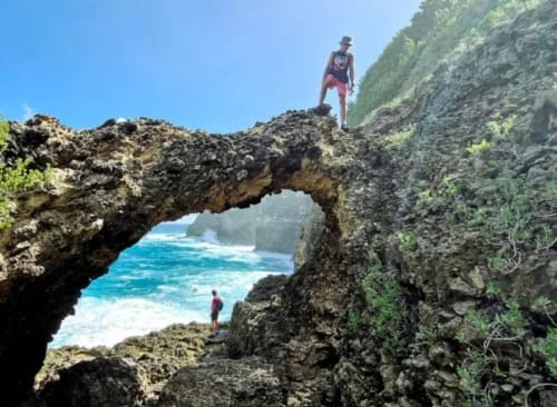 Randonneurs explorant une spectaculaire arche rocheuse surplombant l'océan turquoise près des falaises côtières de la Guadeloupe
