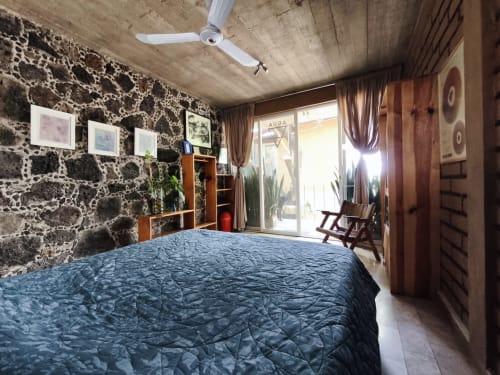 Habitación espaciosa en Casa Santi Tepoz con colcha azul, muros de piedra, ventilador de techo y puertas a patio en Santiago Tepetlapa