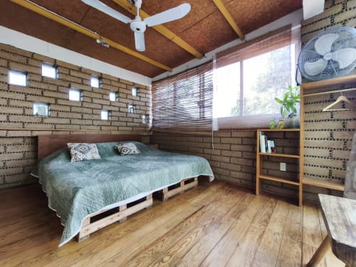Dormitorio rústico en Casa Santi Tepoz con muros de ladrillo, vigas de madera, cama de palés y vistas al jardín en Santiago Tepetlapa