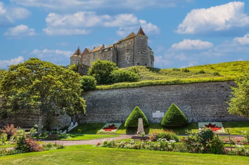 Medieval stone castle surrounded by lush gardens with trimmed hedges, fortified walls, and manicured grounds in Normandy,