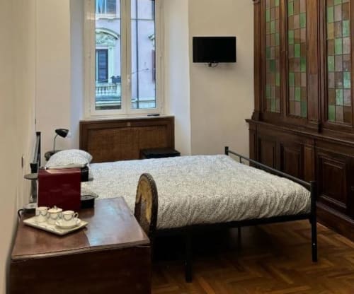 Elegante camera doppia a Domus Giovanna Roma con arredamento in legno, biancheria beige, TV e vista sui monumenti della città