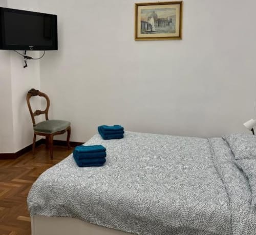 Camera moderna di Domus Giovanna Roma con letto, sedia in legno, TV e stampa architettonica sulla parete