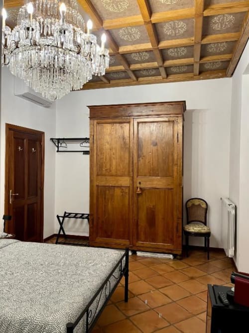 Camera elegante della Domus Giovanna Rome B&B con armadio in legno, lampadario in cristallo e pavimento in cotto