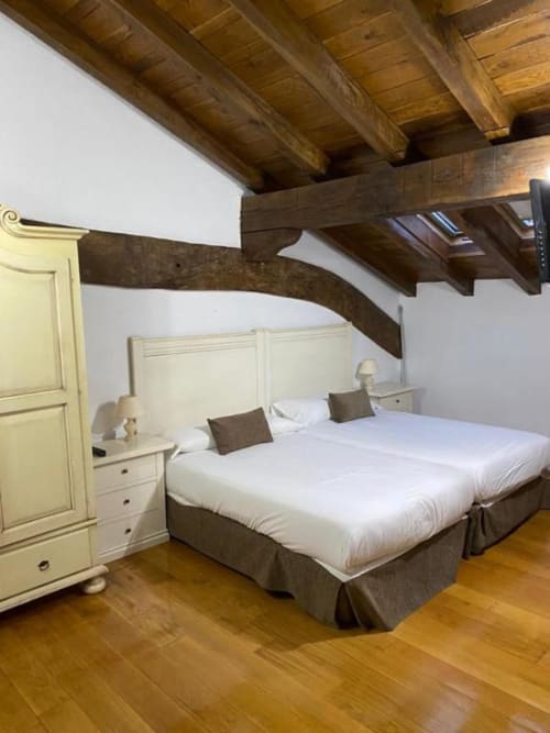 Dormitorio rústico en Casa Rural MAITETXU con vigas de madera vista, cabecero crema, camas gemelas, ropa de cama blanca y detalles en amarillo