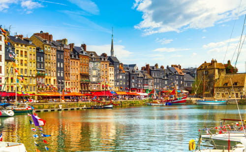 Colorful harbor town with sailboats, historic buildings, and church spire in Normandy, France