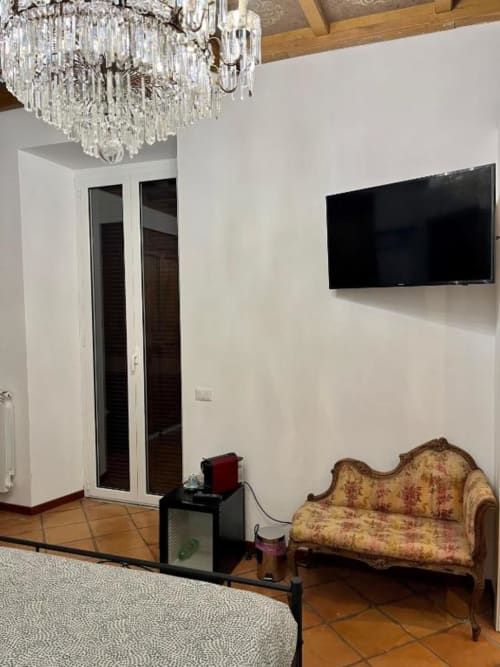 Elegante camera B&B romana con lampadario in cristallo, divano ornato, TV a parete e porte in legno presso Domus Giovanna