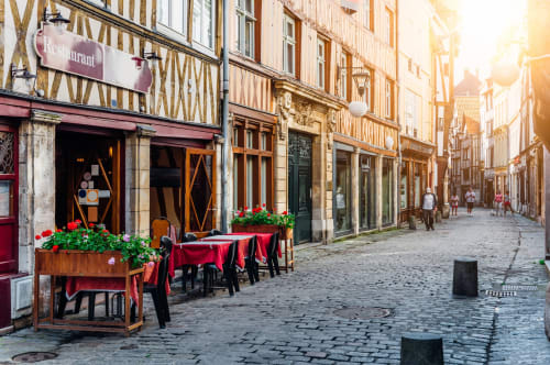 Charming medieval street with half-timbered buildings, outdoor restaurant seating with red tablecloths and flowers in