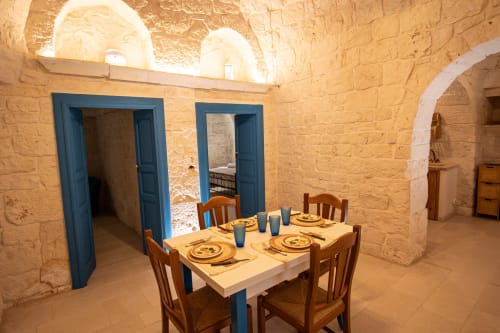 Sala da pranzo nella casa Trulli Life ad Ostuni, con muri in pietra rustica, porte blu e tavolo in legno preparato per gli ospiti
