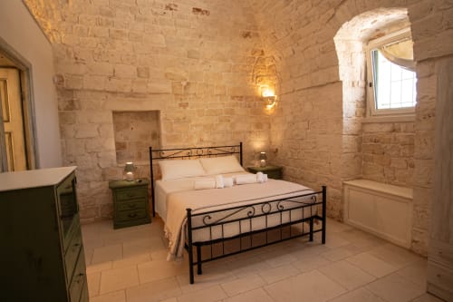 Camera in pietra nella casa Trulli Life di Ostuni, con letto in ferro battuto e finestre ad arco