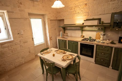 Zona pranzo della cucina rustica del cottage Trulli Life a Ostuni con muri in pietra, mobili verdi e tavolo apparecchiato per tre persone