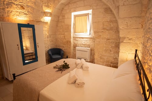 Camera in trullo presso Trulli Life, Ostuni, con muri in pietra, letto bianco, specchio e illuminazione calda