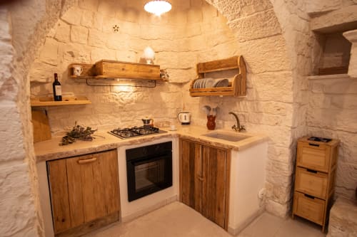 Cucina rustica in trullo a Ostuni con muri in pietra, mobili in legno, fornello a gas e ripiani integrati