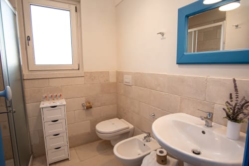 Bagno luminoso della cottage Trulli Life a Ostuni con lavandino, WC, bidet, specchio con cornice blu e dettagli in piastrelle