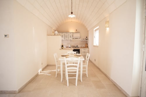 Luminosa sala da pranzo in trullo con tavolo bianco, volta a botte, angolo cucina e luce naturale a Ostuni