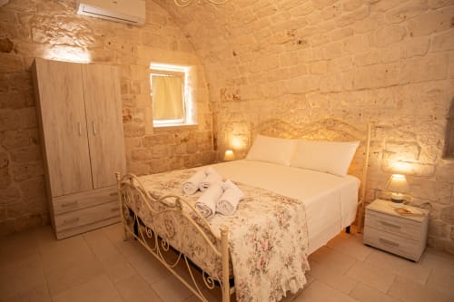 Accogliente camera in trullo a Ostuni con muri in pietra, letto in ferro battuto e illuminazione calda al resort Trulli Life