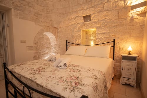 Camera accogliente in una trulli di Ostuni con muri in pietra, biancheria floreale e illuminazione calda