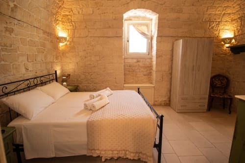 Camera da letto Trulli Life a Bari con muri in pietra, letto in ferro, asciugamani arrotolati e il fascino rustico della Puglia