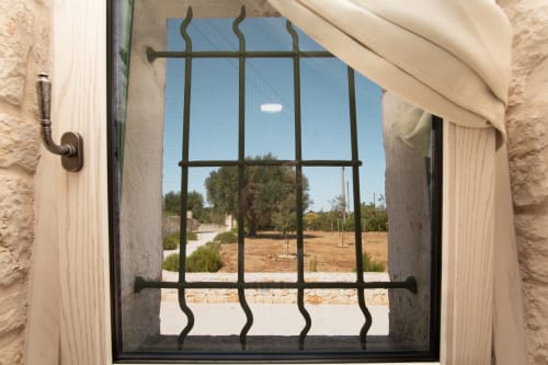 Finestra in ferro decorato con vista sulla campagna dalla camera dell'hotel Trulli Life a Bari, Italia