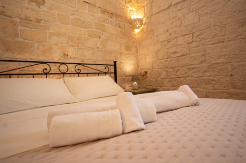 Camera in pietra di Trulli Life Bari con letto in ferro battuto, biancheria bianca, asciugamani arrotolati e illuminazione d'atmosfera