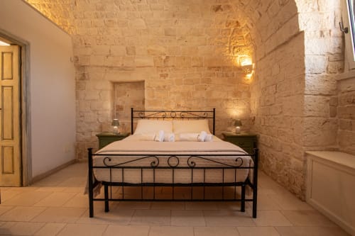 Camera in pietra a Trulli Life a Bari con letto in ferro battuto, illuminazione calda e pavimenti in cotto
