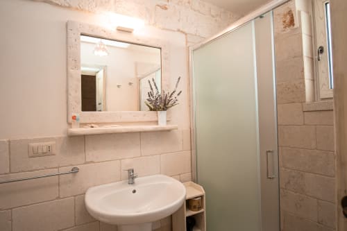 Bagno moderno nella camera Salvia dell'hotel Trulli Life a Bari, con lavabo rotondo, specchio e doccia con piastrelle beige