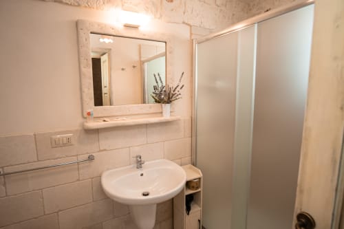Bagno moderno nella camera Salvia dell'hotel Trulli Life a Bari con lavabo bianco, specchio incorniciato, box doccia e piastrelle beige