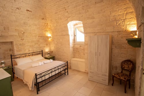 Camera Trulli Life a Bari con muri in pietra, finestra ad arco, letto in ferro, armadio e sedia