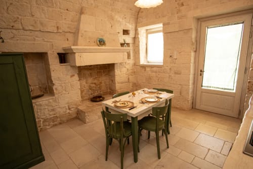 Zona pranzo nella camera Salvia di Trullamie Terra Rossa dell'hotel Trulli Life a Bari, con muri in pietra e sedie verdi