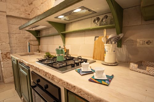 Angolo cucina della camera Terra Rossa Salvia presso l'hotel Trulli Life a Bari, con scaffali verdi e fornello a gas