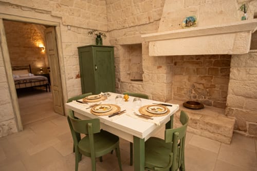 Sala da pranzo di Trulli Life a Bari con muri in pietra, tavolo e sedie verdi, coperto, e ingresso camera da letto