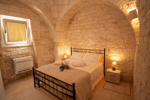 Camera Trulli Life a Ostuni con muri in pietra, letto in ferro battuto e illuminazione calda