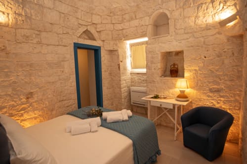 Camera da letto dell'hotel Trulli Life a Ostuni con muri in pietra, letto bianco, scrivania e arredi moderni