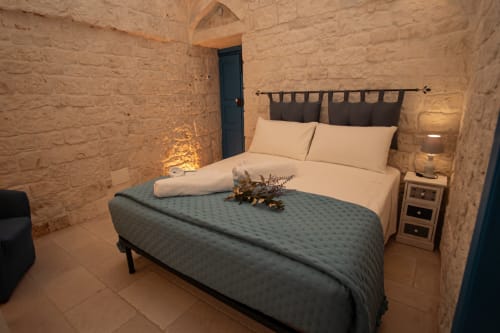 Camera accogliente all'hotel Trulli Life di Ostuni con muri in pietra, letto con cuscini color crema e plaid blu, lampada comodino