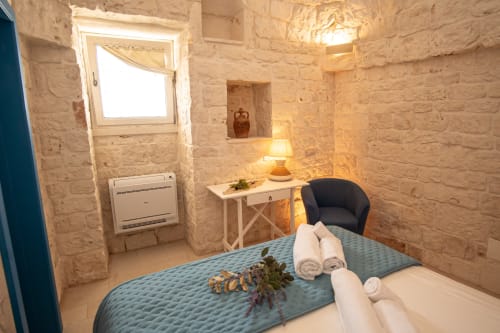 Camera accogliente all'hotel Trulli Life di Ostuni con muri in pietra, letto blu, asciugamani bianchi, lampada da scrivania e finestra