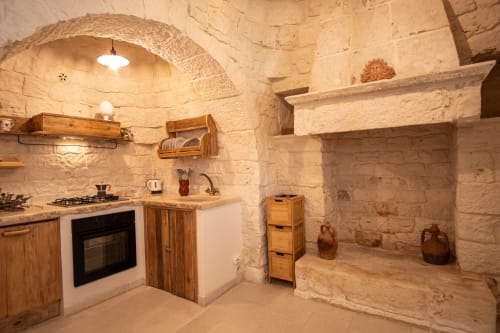 Cucina in pietra tradizionale nella camera dell'hotel Trulli Life, Ostuni, Italia, con soffitto ad arco e arredi in legno
