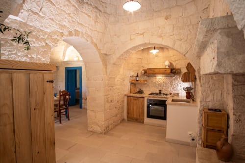 Cucina con muri in pietra nella camera Trullamie Terra Rossa di Trulli Life a Ostuni, con soffitto a volta, mobili in legno e arredamento moderno