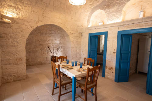 Sala da pranzo Trulli Life a Ostuni con archi in pietra, porte blu e tavolo in legno