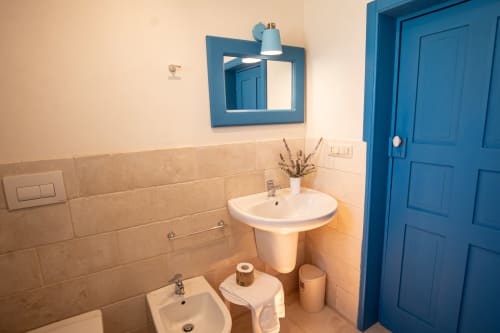 Bagno dell'hotel Trulli Life a Ostuni con specchio dalla cornice blu, lavabo a colonna e porta blu brillante