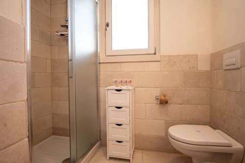 Bagno moderno presso l'hotel Trulli Life di Ostuni con pareti piastrellate, doccia, toilet e armadietto