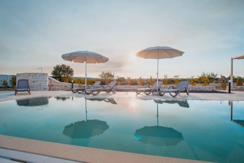 Lussuosa piscina dell'hotel Trulli Life a Ostuni con lettini, ombrelloni e vista sulla campagna all'alba