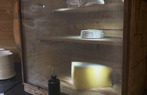 Chez Francine cupboard displaying cheese wheel and yellow container with ambient lighting