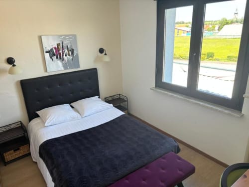 Chambre double moderne à l'Hôtel Restaurant Le S'Y avec tête de lit capitonnée noire, vue sur le jardin par de grandes fenêtres