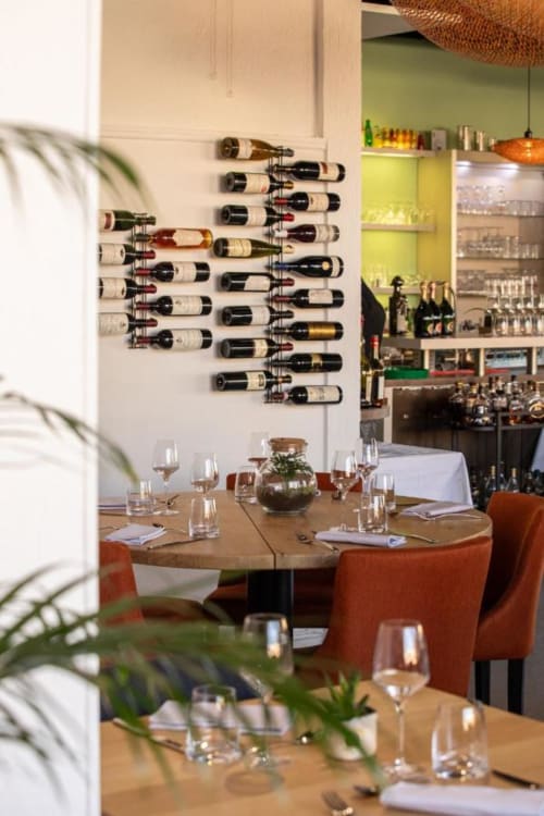 Salle de restaurant contemporaine de l'Hôtel Restaurant Le S'Y avec mur de vins et tables rondes dressées pour le service