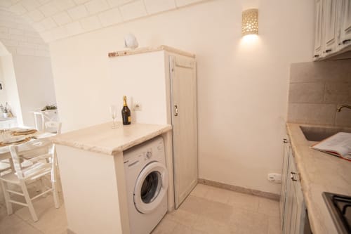 Cucina moderna nella camera dell'hotel Trulli Life di Ostuni, con lavatrice, mobili bianchi e zona pranzo
