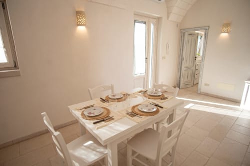 Luminosa zona pranzo presso Trulli Life a Ostuni con tavolo apparecchiato, sedie bianche e luce naturale dalle porte e finestre
